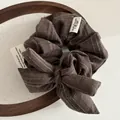 Dettaglio dell'elastico per capelli a righe marrone caffè con fiocco ed etichetta - Marrone