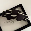 Detail of elegant black fabric bow hair clip with ivory stitching on a display tray - Black