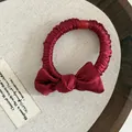 Nahaufnahme eines burgunderroten Satin-Haargummis mit Schleife und roter Perle auf Holz - Steife Schleife Stil / Weinrotes Satinschleife Haargummi