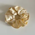 Detailaufnahme des champagnerfarbenen Satin-Scrunchies mit seidiger Textur und Nähten - Milchiges Gelb