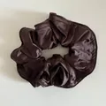 Detailansicht des dunkelbraunen Satin-Haargummis mit feiner Naht und plissierter Textur - Braun