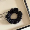 Détail d'un chouchou en satin noir plissé avec texture soyeuse dans un écrin bijou - Noir