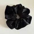 Detail of a large black satin scrunchie showing smooth texture and ruffled edges - Black