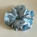 Detailed view of large light blue satin scrunchie with smooth texture and soft pleats - Blue