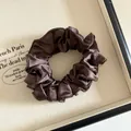 Détail d'un chouchou en satin marron foncé avec des plis denses et une texture soyeuse - Marron