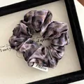 Macro shot of purple and brown marble pattern velvet scrunchie with brand logo tag - Purple