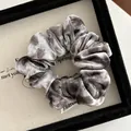Macro shot of a grey velvet scrunchie with soft sheen and woven brand label on white card - Brown