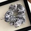 Detailed view of gray velvet leopard print scrunchie with FMdrea logo tag in a box - Gray