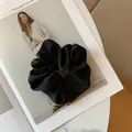 Detail of a large black satin silk scrunchie with natural pleats on a fashion magazine - Black