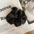 Detailed view of black satin scrunchie with subtle texture on a fashion magazine - Black