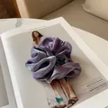 Détail d'un chouchou en satin violet brillant avec finition irisée posé sur un magazine - Violet Marbré
