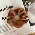 Détail d'un chouchou en satin marron caramel avec texture gaufrée posé sur un magazine - Café Clair