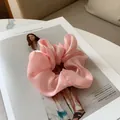 Vue détaillée d'un chouchou en satin rose posé sur le fond d'un magazine de mode - Rose