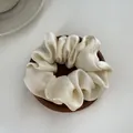 Detailopname van een crème satijnen scrunchie met zijdezachte plooien op hout - M / Broken Wit