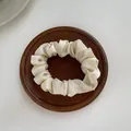 Detailopname van crème satijnen scrunchie met zijdezachte plisséstructuur op hout - S / Broken Wit