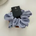 Close-up of light purple satin scrunchie with rhinestones on a wooden display base - Blue