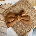 Classic brown faux leather bow hair clip placed on a rustic straw mat background - Light Camel