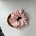 Pink satin silk scrunchie with smooth pleated texture on a round wooden tray - Pink