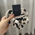 French style scrunchie with cow pattern print on smooth satin fabric held by hand - White Base Cow Print / White