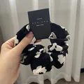 Detail of a black and white floral scrunchie with a brand tag on a soft background - Black Base Floral/Cow Print / Black