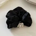 Detalle de un coletero de satén negro con una flor de camelia brillante con pedrería fina - Negro