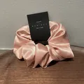 Detailopname van een roze satijnen scrunchie op een houten dienblad met merklabel - Roze