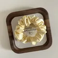 Elegant cream yellow satin silk scrunchie with smooth pleated texture on wood tray - S / Yellow