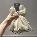 Dettaglio di scrunchie in organza crema con bordo nero e strati plissettati eleganti - Bianco Sporco