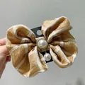 Macro detail of plaid fabric bow hair clip with central pearl and rhinestone embellishment - Turmeric