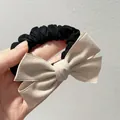 Detail view of a large cream bow hair tie with black pleated elastic band held in hand - Apricot