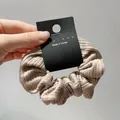 Close-up of beige ribbed fabric hair scrunchie with nyu·nyu retail tag detail - Khaki Medium