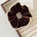 Detailed shot of dark brown velvet scrunchie with lace edges and handmade gold charm - Brown