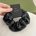 Close-up of black faux leather scrunchie with soft pleats and modern texture detail - Black
