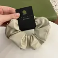 Detail shot of a cream faux leather scrunchie with visible texture and branded tag - Grey-Beige