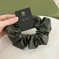 Close-up of olive green PU leather scrunchie on display card showing glossy pleated texture - Antique Green