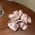 Macro detail of champagne pink satin scrunchie with layered ruffles on a wooden background - Aurora Pink
