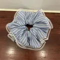 Detalle de coletero de tela a rayas azules con borde de encaje blanco sobre madera - Raya Azul
