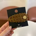 Bruine strik haarklem met gouden smiley bedeltje op een presentatiekaart - Lachend Gezicht BB Clip