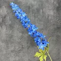 Vibrante blaue künstliche Rittersporn-Blume mit grünen Blättern auf dunklem Hintergrund - Blau