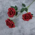 Three deep red artificial roses with green leaves on a gray textured background - Red