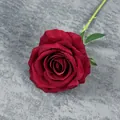 Deep red velvet artificial rose with green leaves on a dark textured background - Dark Red