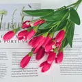 Künstlicher rosa Tulpenstrauß mit Seidenblüten und grünen Stielen auf einem Magazin - Rosenrot