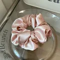 Detailopname van een hoogwaardige lichtroze satijnen scrunchie met een zachte zijdeachtige glans - Roze Middel