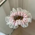 Detail eines rosa Satin-Haargummis mit weißem Organza-Spitzenrand auf spiegelnder Fläche - Rosa