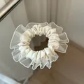 Detailansicht eines cremefarbenen Organza-Haargummis mit Rüschen auf Spiegelfläche - Cremeweiß