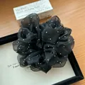 Detail von schwarzem Organza-Haargummi mit glitzernden Strasssteinen auf Holztisch - Haargummi Mit Weißem Diamanten