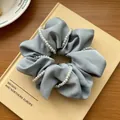 Detalle de coletero de satén gris con cadena de perlas elegantes sobre un libro - Azul