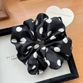 Detailopname van een zwart-witte polkadot satijnen scrunchie op een wit dienblad - Zwart