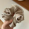 Close-up of a large champagne satin scrunchie with elegant white contrast piping - Khaki
