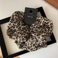 Detail of leopard print satin scrunchie with brand tag inside a black frame - Brown Leopard